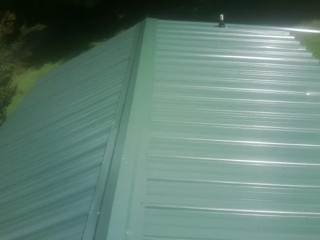 New green metal panels meeting at the ridge of a roof — Flat Roof Repair work by our crew in Richmond