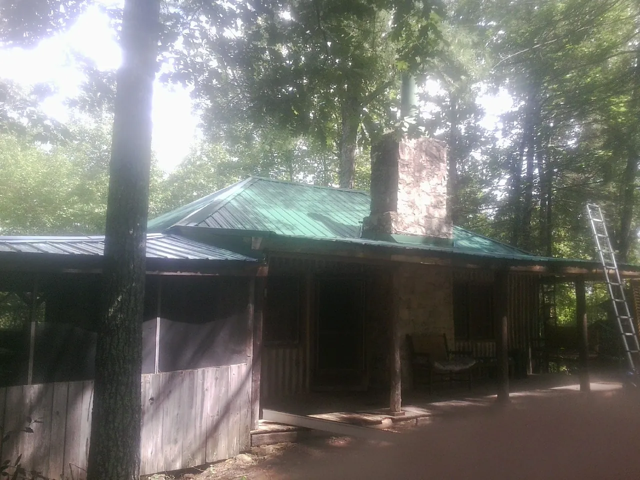 Green metal roof and stone chimney above a log cabin porch in Richmond